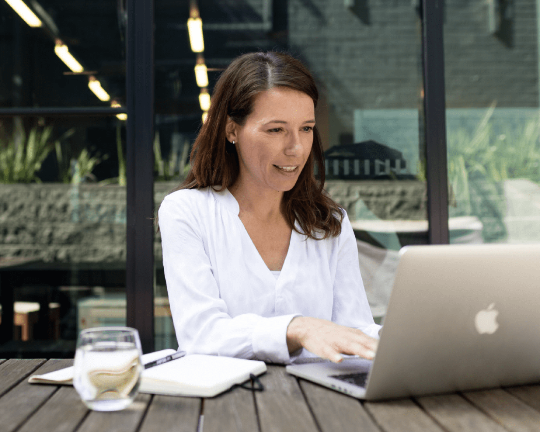 Woman using Xero’s accounting software for lawyers on a laptop outdoors with notebook and water glass.